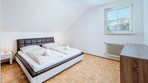 A bedroom with a bed, a nightstand, a lamp, a window with a view, and a radiator. - Ferienwohnung Grimmingblick by Interhome (Öblarn)