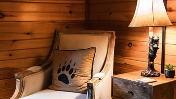 A wooden-paneled room with a plush armchair featuring a paw print cushion, a small table with a lamp and a decorative statue, and a television mounted on the wall.