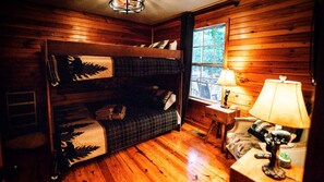 Een gezellig vakantiehuisje met een stapelbed, een kleine tafel met een lamp, en een raam met uitzicht op bomen.