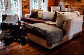 A cozy living room with a sofa, a chair, and a coffee table. There is a window with a view of trees.
