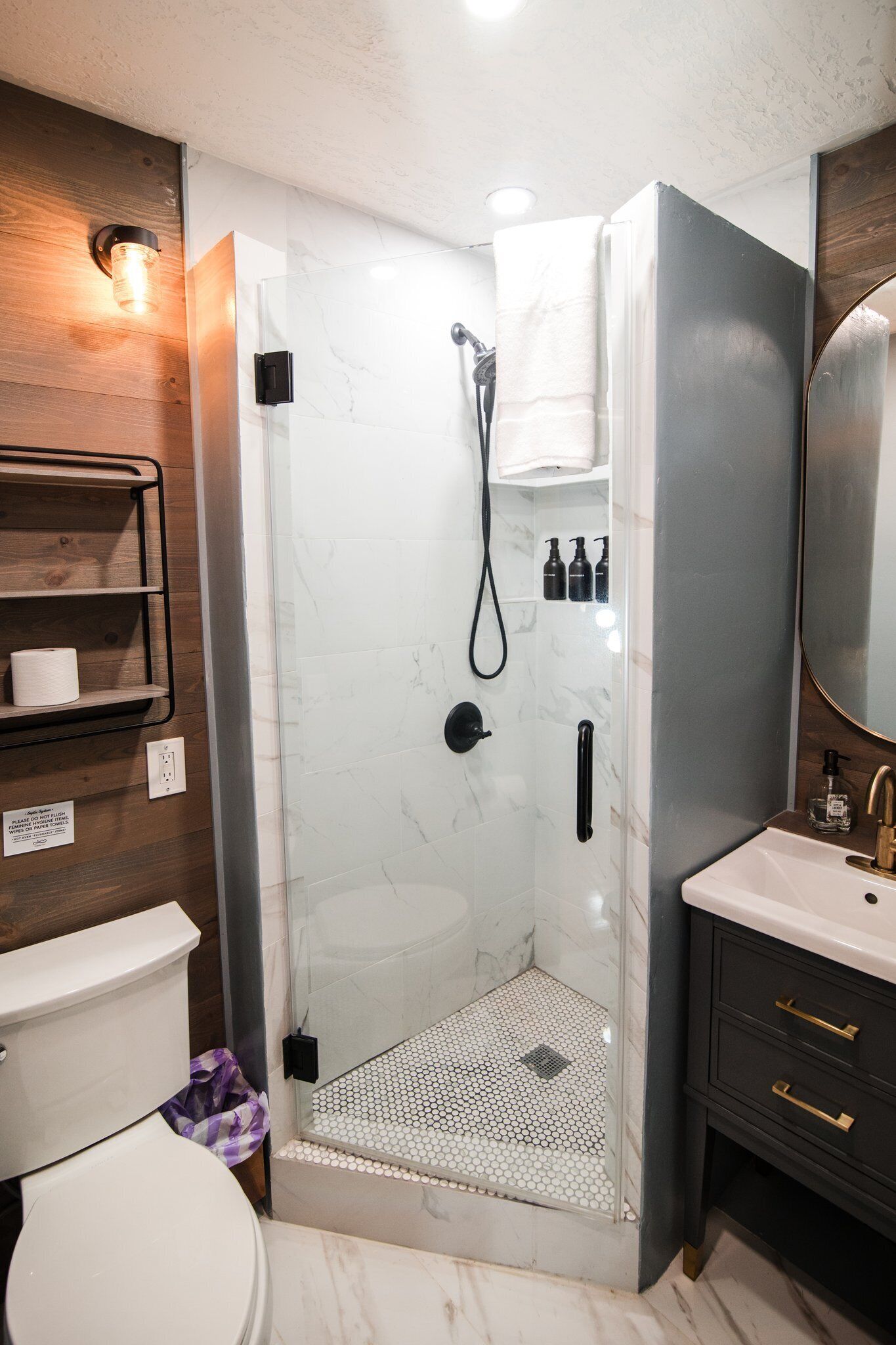 A modern bathroom with a glass-enclosed shower, a white toilet, and a vanity with a mirror.