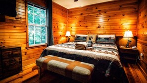 A wooden-paneled room with a bed, two bedside lamps, a bench, and a window.
