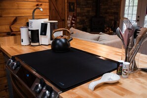 Une cuisine équipée d’une cuisinière, d’une machine à café, d’une bouilloire et d’ustensiles de cuisine, le tout posé sur le plan de travail.