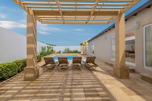 A covered outdoor patio with a pool, lounge chairs, and a pergola.