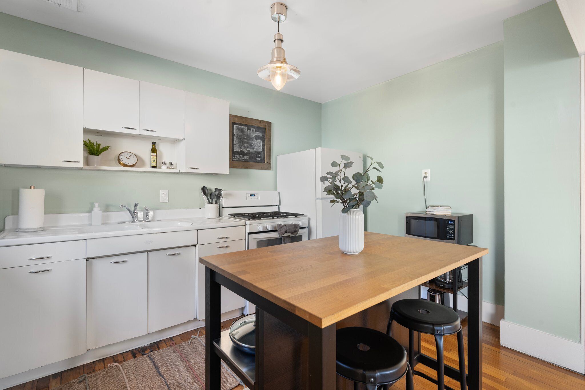 A modern kitchen with white cabinets, a wooden table, and a microwave.