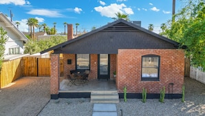 Une petite maison en briques avec un patio, une allée en gravier et une clôture en bois.