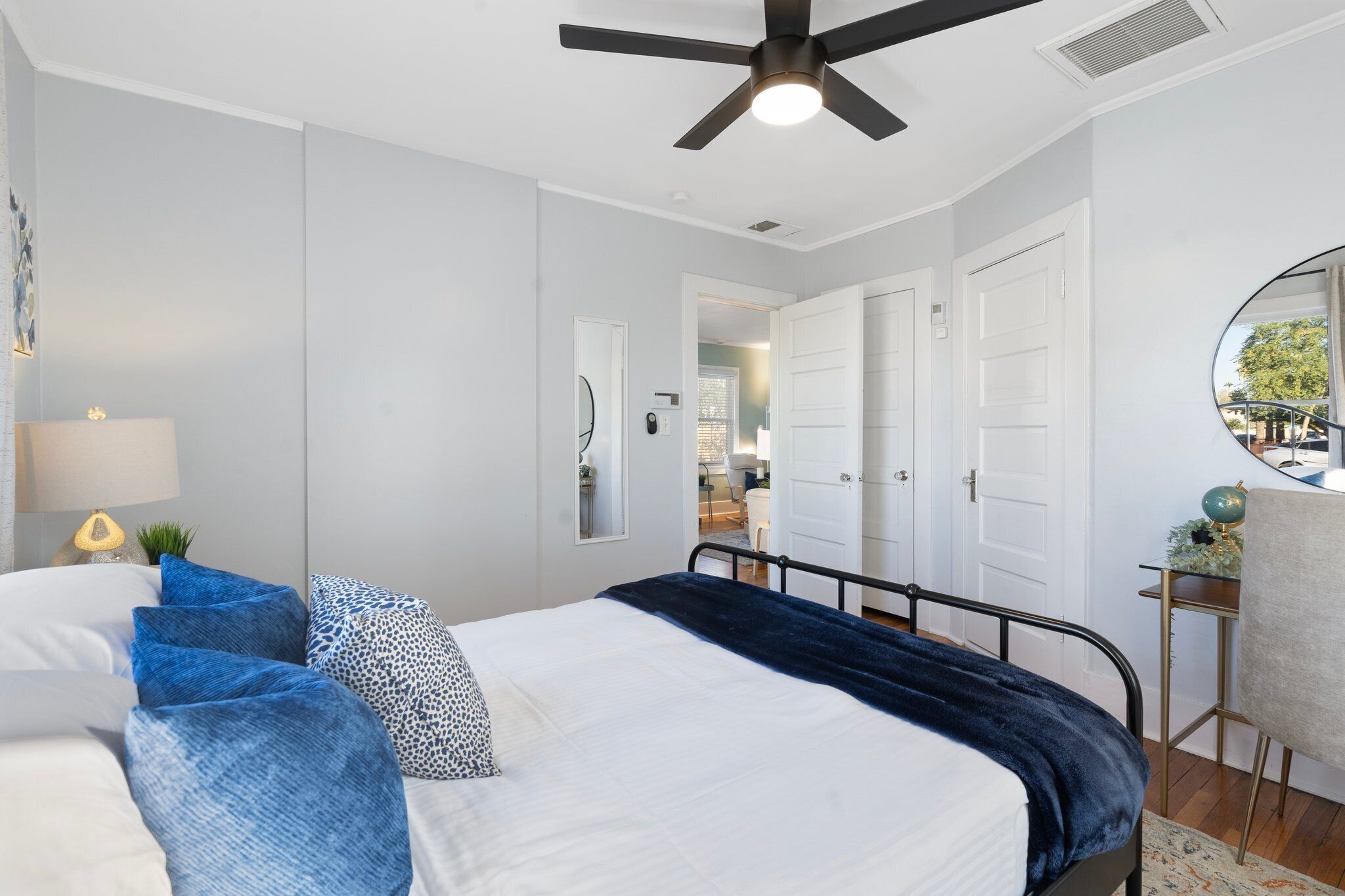 A bedroom with a bed, a ceiling fan, a nightstand with a lamp, and a view of a hallway with doors.