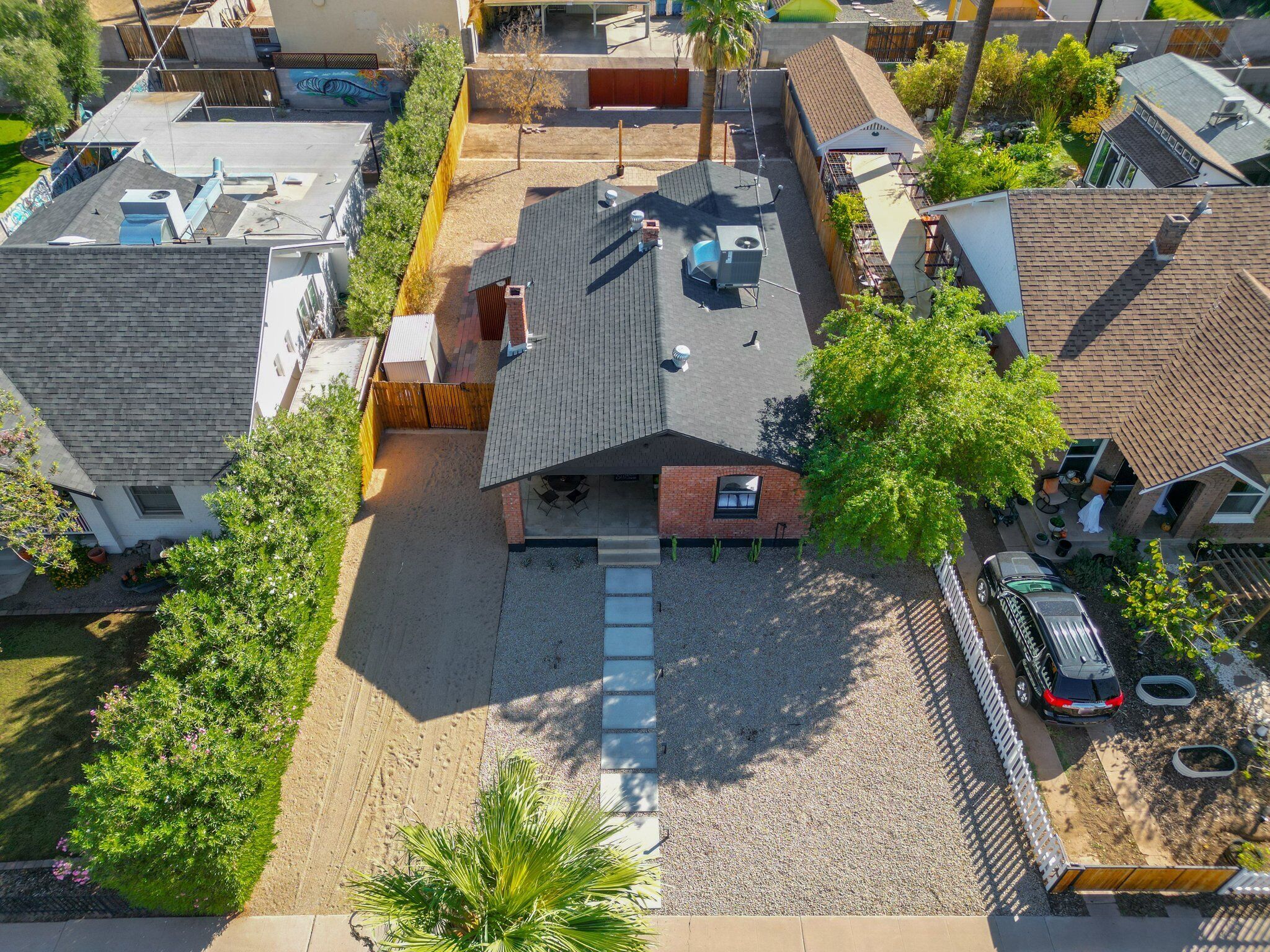 An aerial view of a residential area with a house featuring a sloped roof, a patio with outdoor furniture, and a fenced yard.