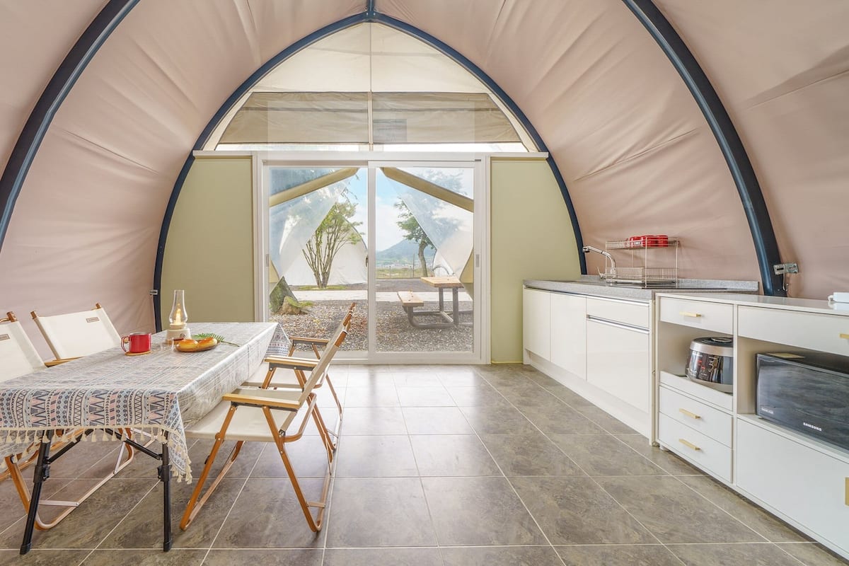 Une tente comprenant un espace repas, une cuisine et offrant une vue sur l’extérieur.