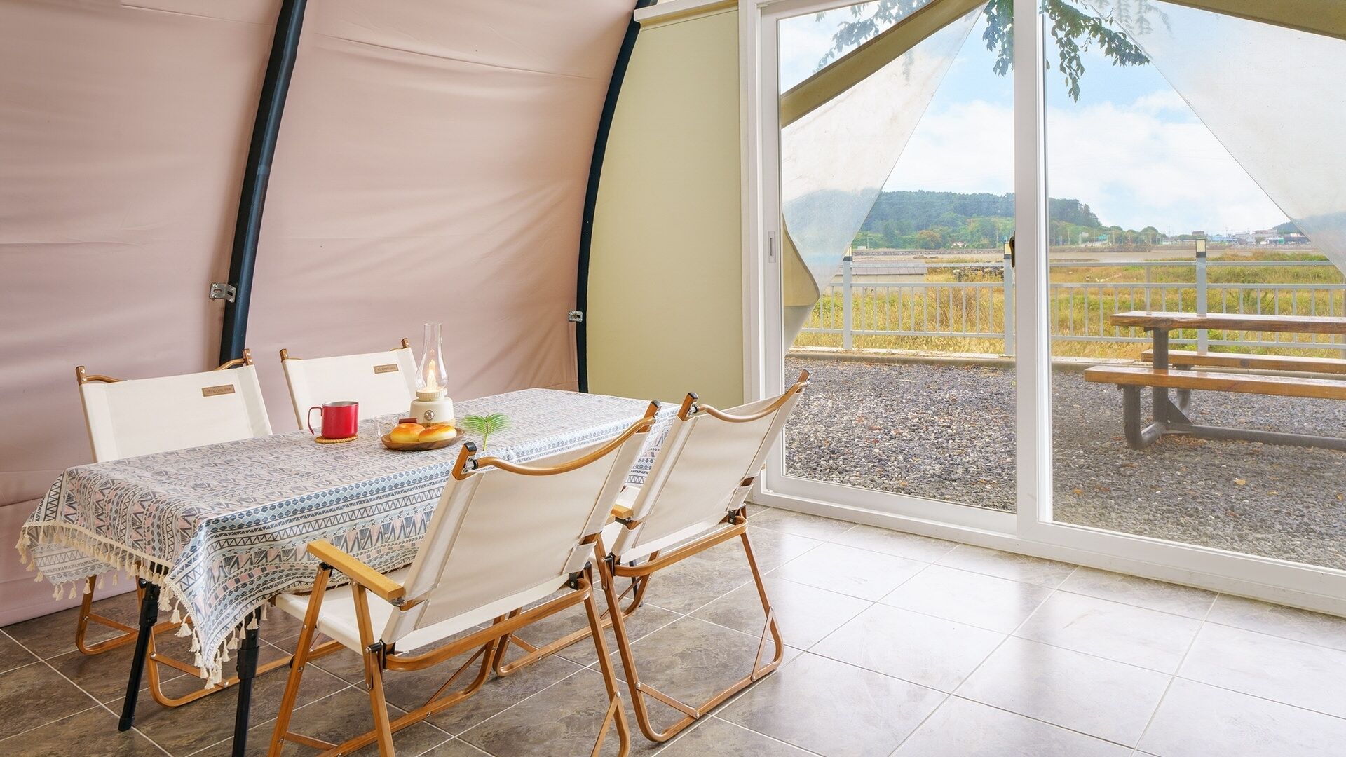 Una habitación con carpa, una mesa, sillas, una lámpara y vistas a un parque.