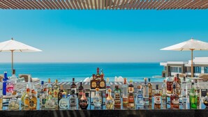 Een bar met verschillende drankflessen en parasols met uitzicht op een heldere blauwe oceaan.