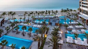 Een resort met meerdere zwembaden, palmbomen en uitzicht op het strand.