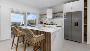 A modern kitchen with a large island, bar stools, a stainless steel refrigerator, and a view of the city. - Spectacular View  Private Pool  King Beds  Ensuite (Noord)