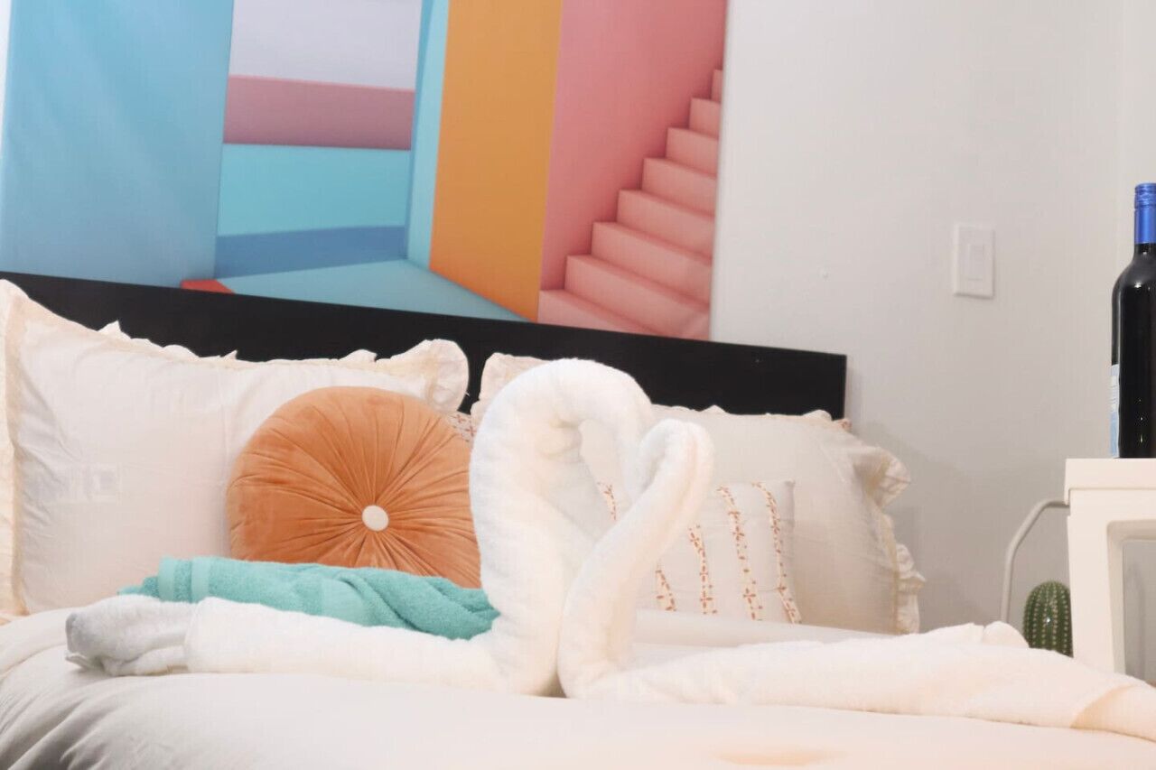 A bed with white and orange pillows, a teal blanket, and a white swan-shaped pillow.
