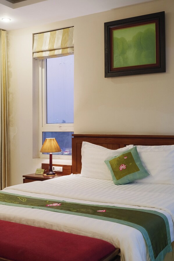 A neatly made bed with a green and red bedspread, a single pillow with a floral design, and a framed picture on the wall. - Ngan Ha Hotel (Hanoi)