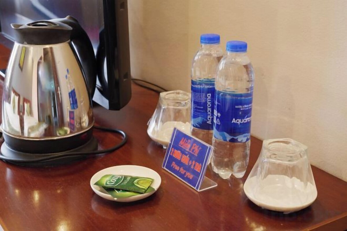 A hotel room table with a kettle, two water bottles, a glass, a plate with a packet, and a sign.