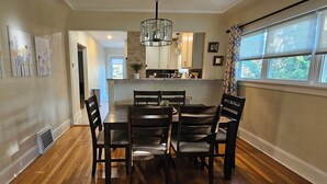 A dining area with a wooden table and chairs, a hanging light fixture, and artwork on the walls.