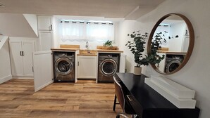 A compact kitchen with two washing machines, a sink, and a mirror.