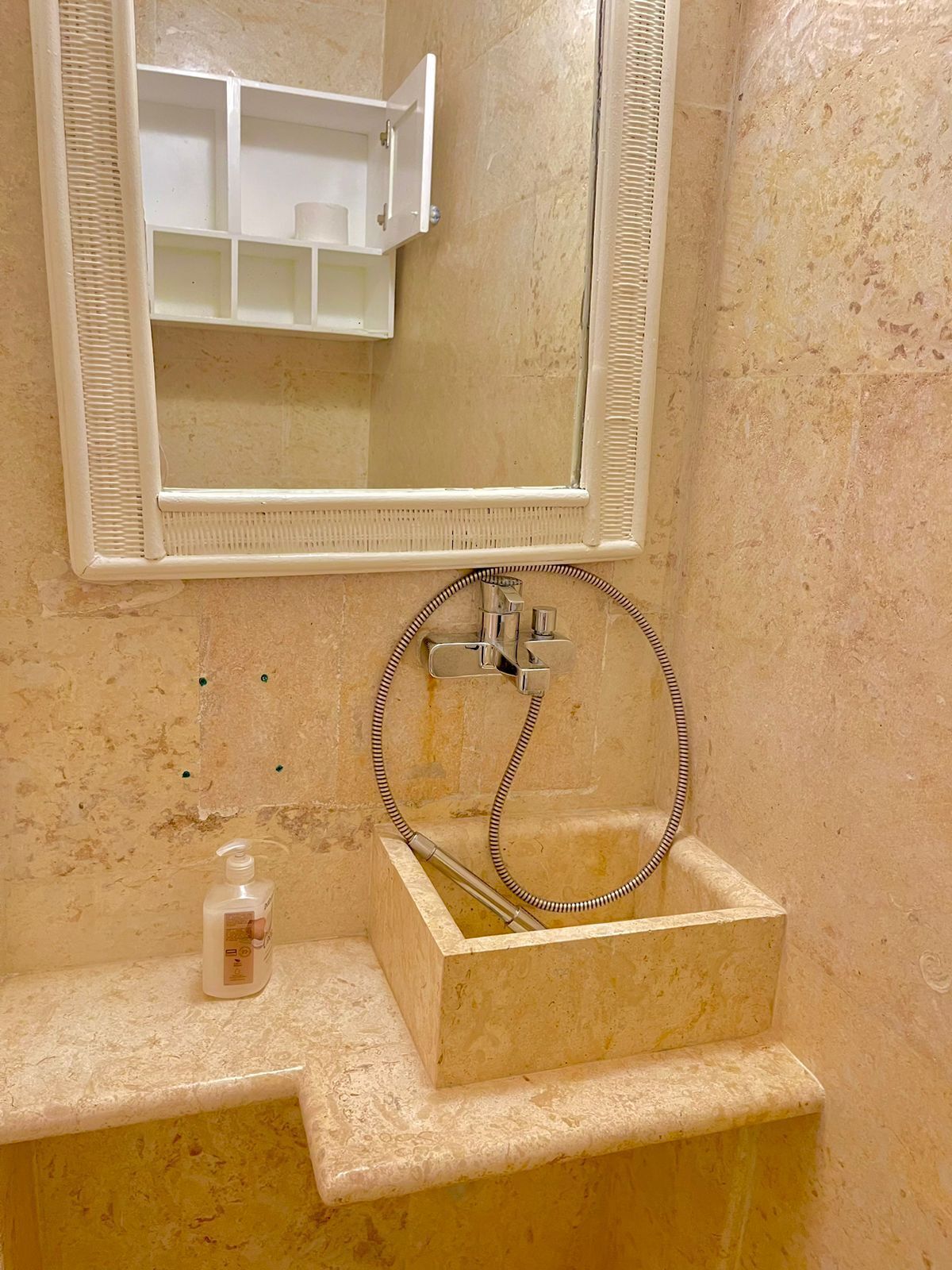 Ein Badezimmer mit einem rechteckigen Waschbecken, einer Handbrause und einem Spiegel über dem Waschbecken.