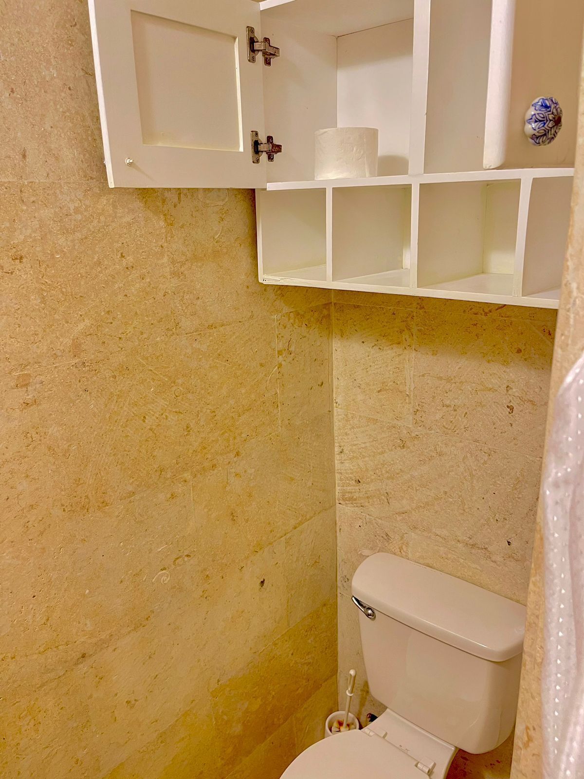 Une salle de bain avec des toilettes, une étagère sur laquelle se trouve un rouleau de papier toilette et un objet décoratif accroché au mur.