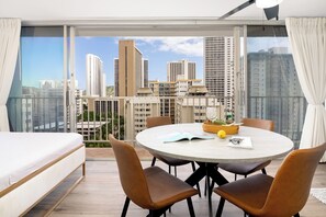 A modern hotel room with a large balcony, a round dining table, and a bed.