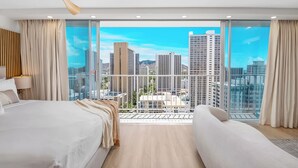 Une chambre d’hôtel moderne avec un grand lit, un petit canapé et un balcon offrant une vue sur la ville.