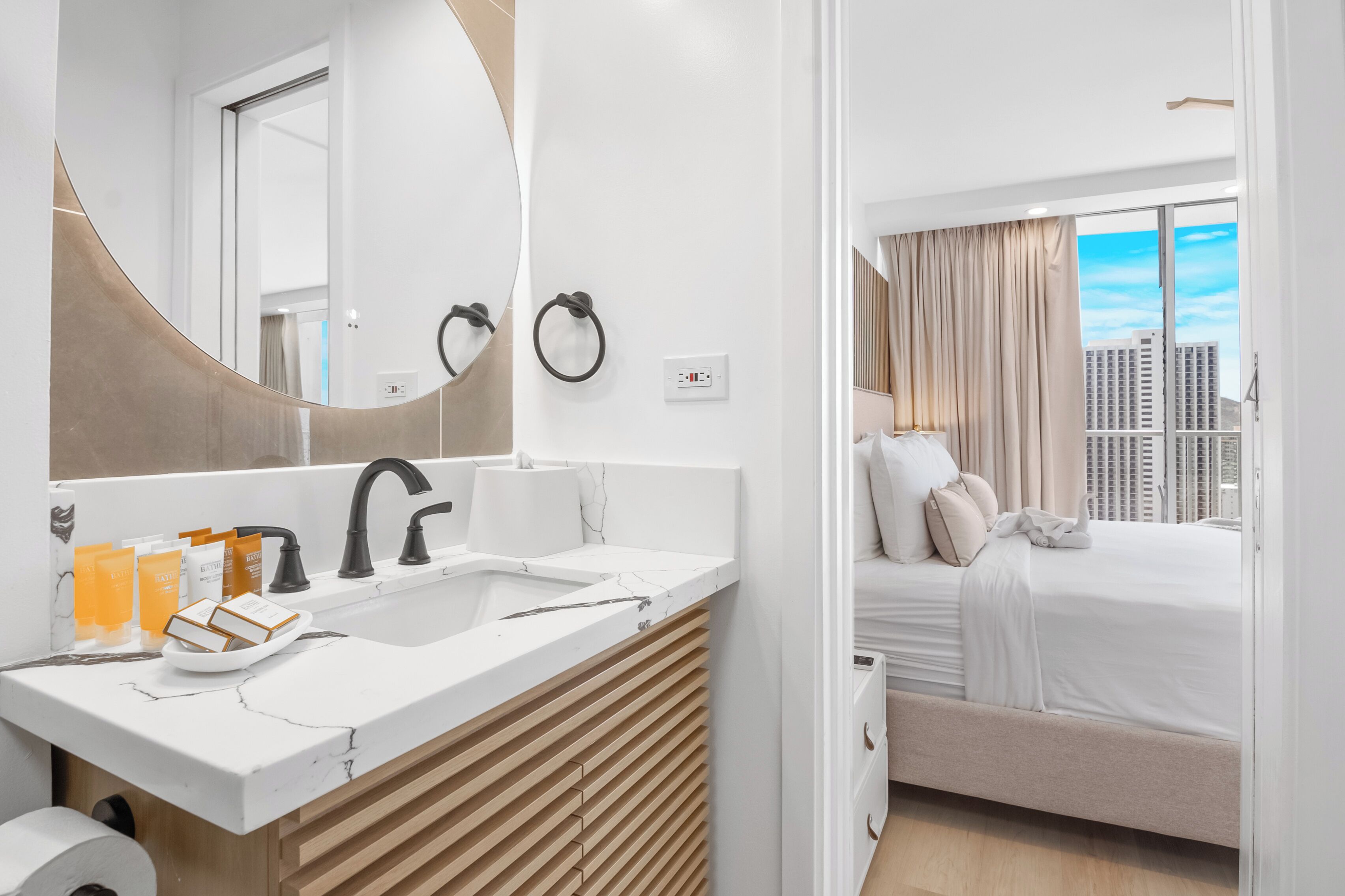 Een moderne hotelkamer met een groot bed, een badkamer met een marmeren wastafel en uitzicht over de stad.