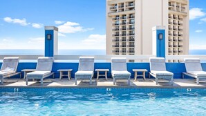 Un espace piscine aménagé sur le toit, avec des chaises longues et une vue sur un grand immeuble.