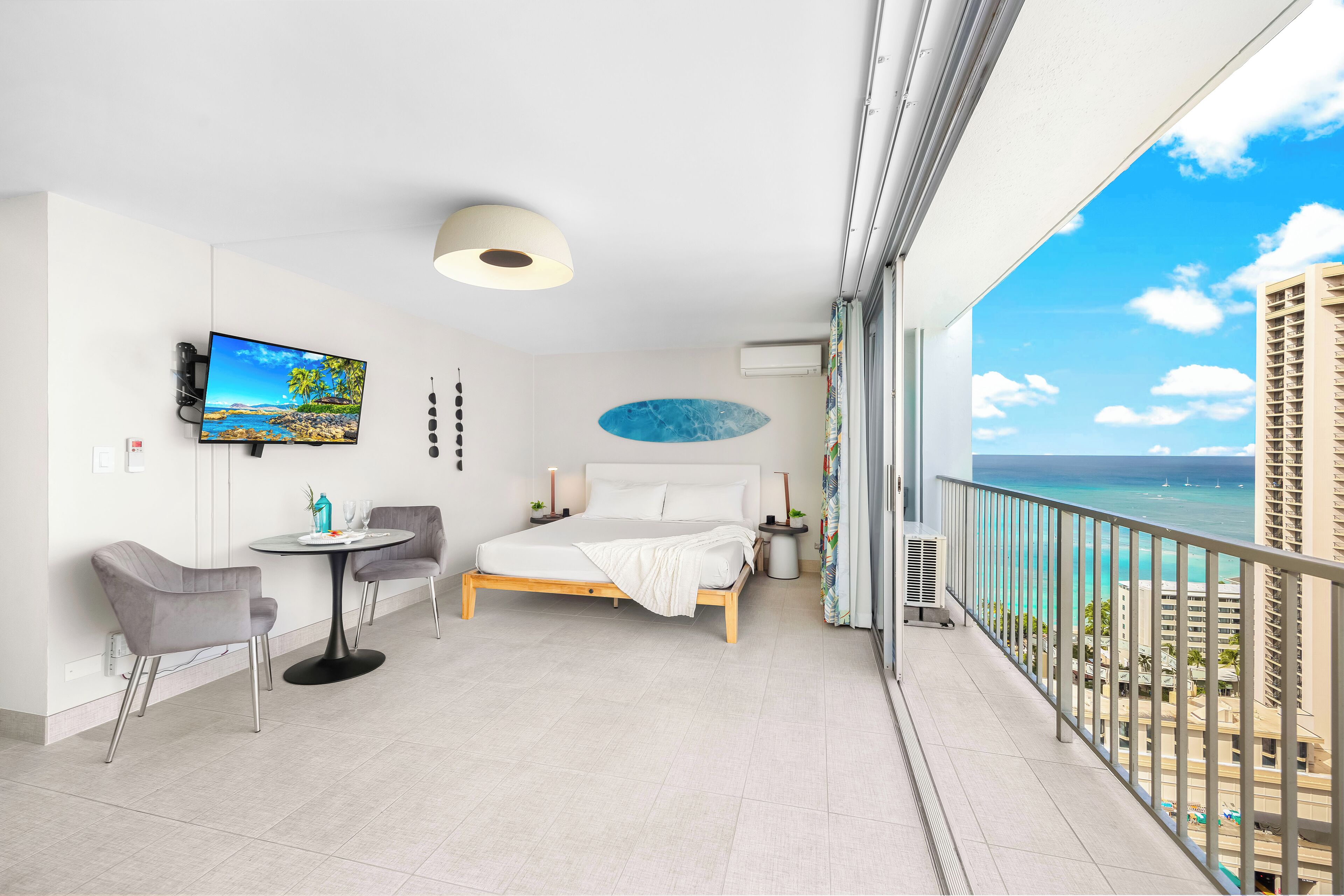 Ein Hotelzimmer mit Bett, Fernseher, einem Balkon mit Meerblick und einem Essbereich mit Stühlen und Tisch.