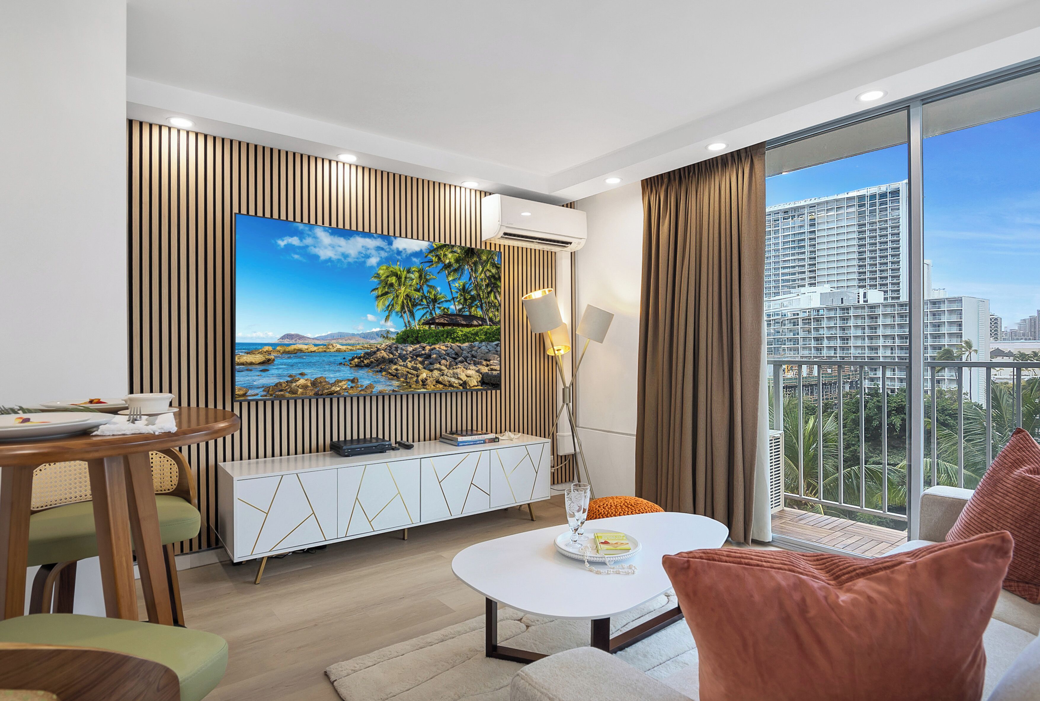 A modern living room with a large flat-screen TV, a dining area, and a balcony with a city view.