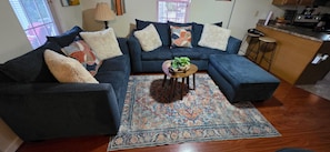 A living room with a blue sofa, patterned rug, and a small wooden table with a plant.