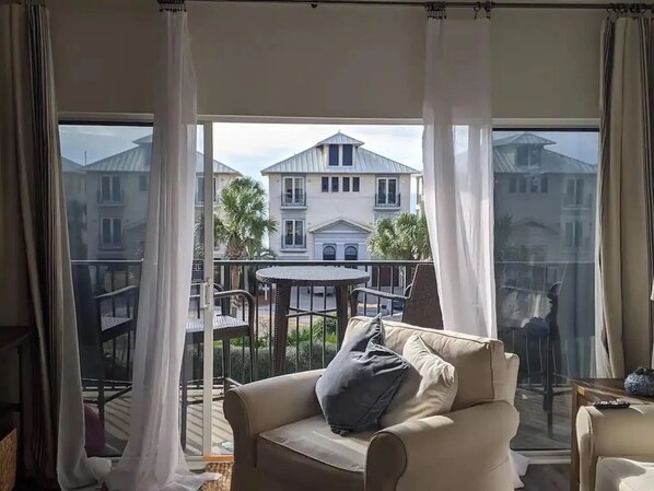A balcony with a view of a white building, a round table, and a beige sofa.