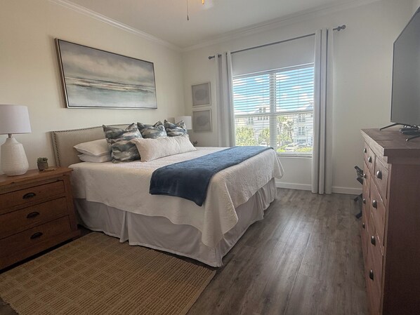 A bedroom with a bed, nightstands, a dresser, a window with curtains, and a painting on the wall.
