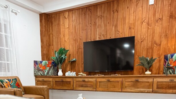 Ein modernes Wohnzimmer mit einer Holzpaneelwand, einem Flachbildfernseher, einem türkisfarbenen Couchtisch und einem gemusterten Teppich.
