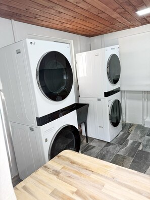 A laundry room with stacked LG washing machines and dryers, wooden ceiling, and tiled floor. - Harbor Haven Luxury Retreat I- VEHICLE INCLUDED (St. George)