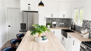 Eine moderne Küche mit weißen Schränken, einer zentralen Kochinsel, einem Edelstahlkühlschrank, einer Kaffeemaschine und einem Spülbecken.