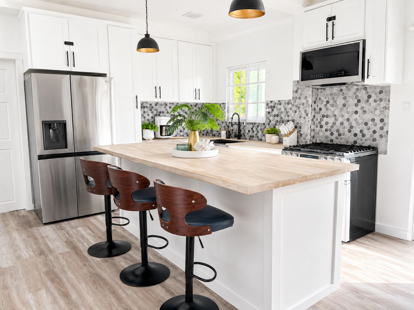 Una cocina moderna con una isla central, taburetes de bar, electrodomésticos de acero inoxidable y un salpicadero con azulejos hexagonales.