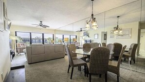 A spacious living room with a large sofa, dining table, wicker chairs, and a ceiling fan.