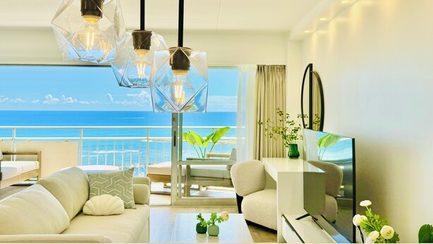 A modern hotel room with a balcony, a sofa, a coffee table, and a TV. - Panoramic Oceanview Home (Car Available) (Honolulu)
