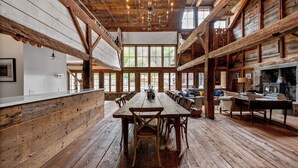 A rustic dining area with a long wooden table, multiple chairs, and a chandelier. - Renovated Grand Woodstock Barn (Bearsville)