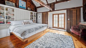 A bedroom with a wooden bed, white shelving, a large window, and a red chair. - Renovated Grand Woodstock Barn (Bearsville)