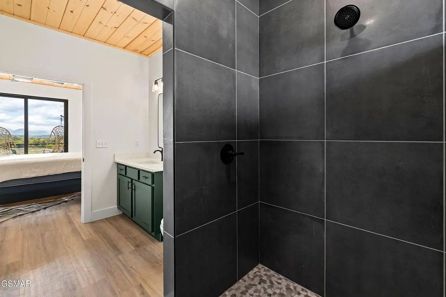 A modern bathroom with dark tiles, a shower, and a view of the outdoors.