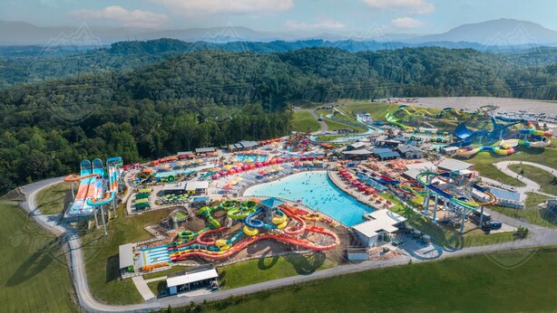 Luftaufnahme eines Wasserparks mit mehreren Wasserrutschen, einem großen Schwimmbecken und umgebender Bepflanzung.