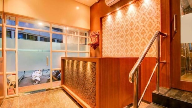 A reception area with a wooden reception desk, a patterned wall, and a staircase. - Glitz Hotels AR Residency (Thane)