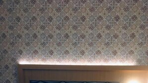 A hotel room with a bed, a headboard, a nightstand, and a wall with patterned wallpaper. - Glitz Hotels AR Residency (Thane)