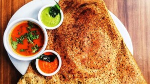 A plate with a folded dosa, two chutneys, and a small bowl of sauce. - Glitz Hotels AR Residency (Thane)