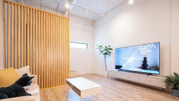 A modern living room with a sofa, a white coffee table, a TV on a stand, and a wooden partition. - REPOS tsuruhashi (Osaka)
