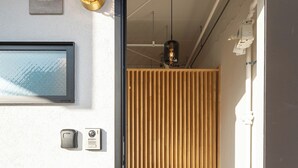 A modern entrance with a wooden slat door, a framed picture, and a wall-mounted light fixture. - REPOS tsuruhashi (Osaka)