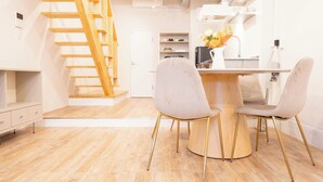 A modern kitchen with a wooden staircase, a dining area with two chairs, and a small island with a vase of flowers. - REPOS tsuruhashi (Osaka)