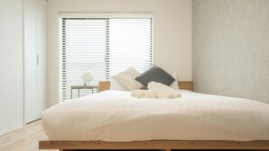 A bedroom with a wooden bed, white bedding, and a window with blinds. - REPOS tsuruhashi (Osaka)